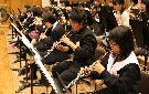 段前列で演奏する木管楽器の学生ら